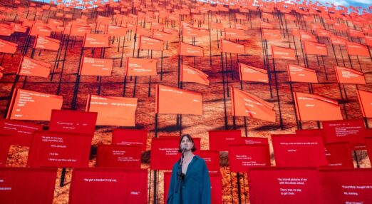 Caitlin O'Ryan in front of a mic. Behind her are hundreds of red flags.