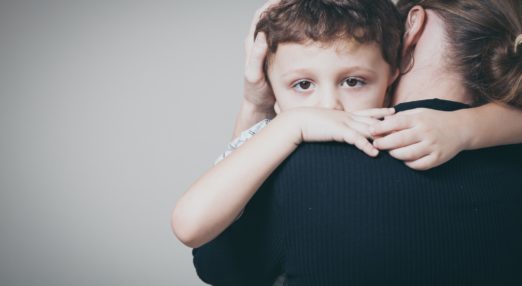 Image of the back of an adult woman holding a child who is looking into the camera