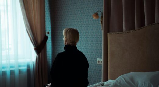 Woman sat on bed, facing towards window and away from the camera