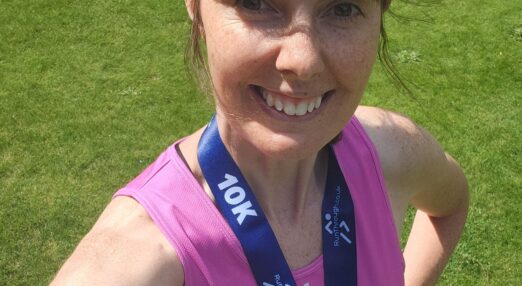 Selfie of Alison May smiling at the camera in a Refuge running vest wearing a medal