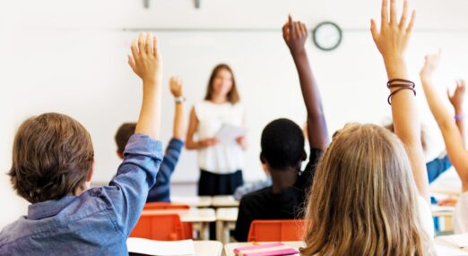 School children put up hands in a classroom