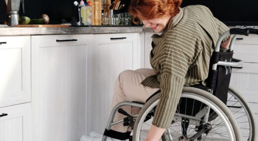 Woman in kitchen leans over her wheelchair to pet a cat
