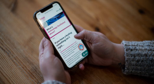 Close up of a hand holding a phone. Webpage displays Refuge's tech Abuse website.