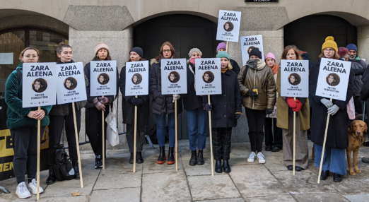 Women holding placards that show a photo or Zara Aleena and her name stand in front of a building that says Central Criminal Court. Everyone is wrapped up against the cold and the mood is sober.